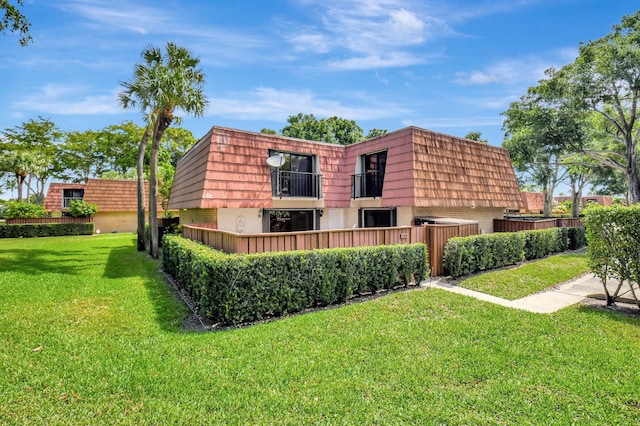 view of side of property featuring mansard roof, a balcony, brick siding, and a lawn