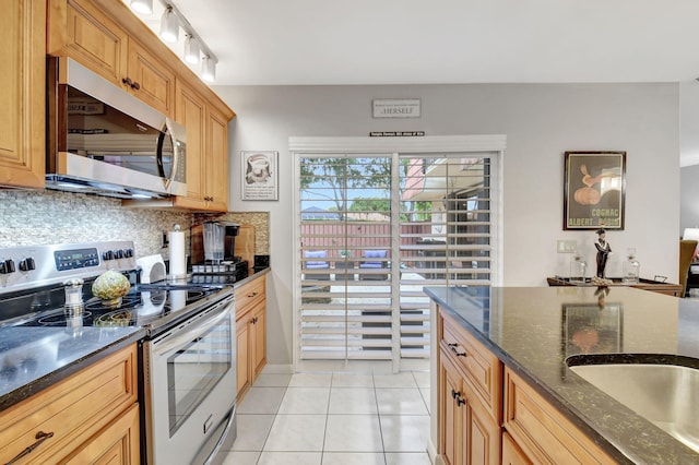 kitchen with appliances with stainless steel finishes, backsplash, light tile patterned floors, and dark stone countertops