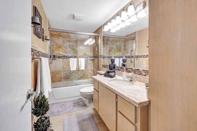 bathroom with tile walls, vanity, toilet, shower / bath combination with glass door, and tile patterned floors
