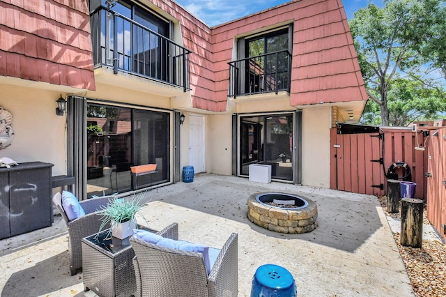 back of property featuring a balcony, an outdoor fire pit, mansard roof, a gate, and a patio