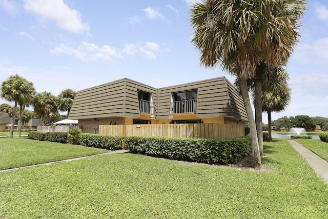 view of front of home featuring mansard roof, brick siding, a front lawn, and a balcony