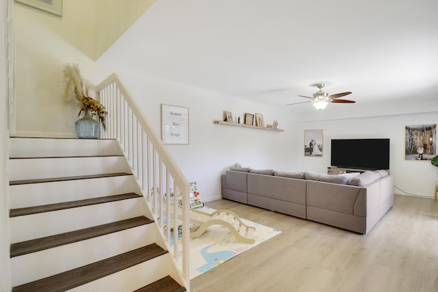 living area featuring wood finished floors, ceiling fan, and stairway