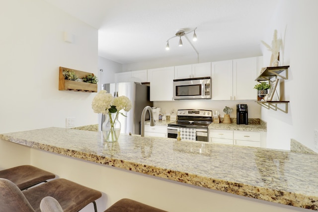 kitchen with stainless steel appliances, a peninsula, light stone counters, a kitchen bar, and white cabinets
