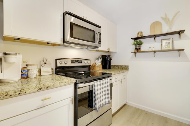 kitchen featuring appliances with stainless steel finishes, light wood finished floors, white cabinetry, light stone counters, and baseboards