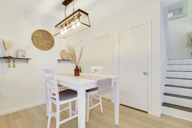 dining area featuring light wood-style floors, a chandelier, baseboards, and stairs