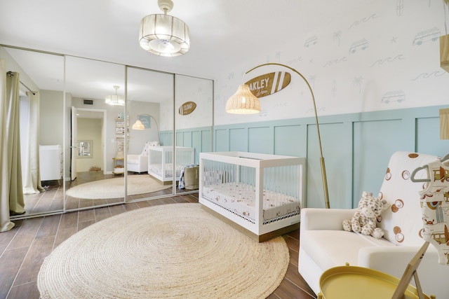 bedroom featuring wainscoting, a closet, wood finished floors, wallpapered walls, and a decorative wall