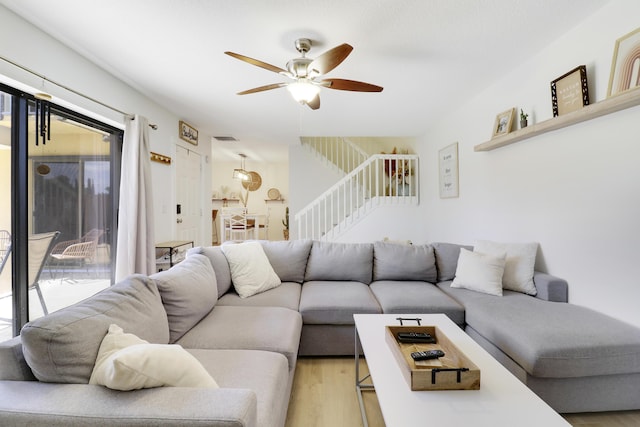 living room with a ceiling fan, light wood finished floors, and stairway