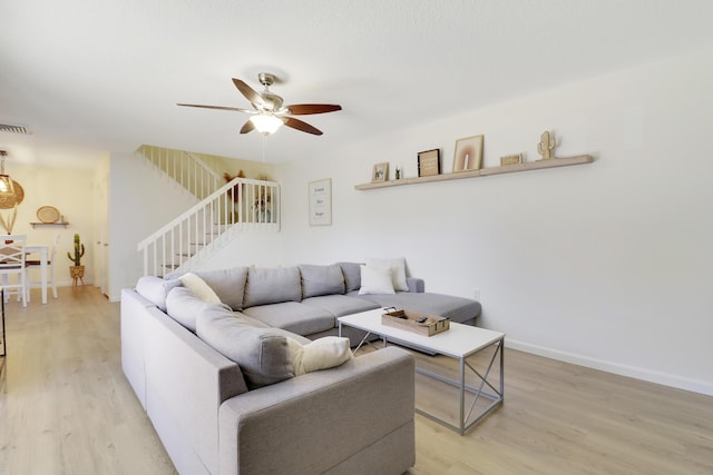 living area featuring light wood finished floors, ceiling fan, stairs, and baseboards