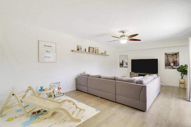 living area with light wood-style floors, a ceiling fan, and baseboards