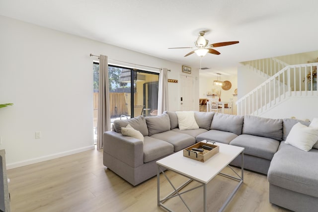 living area featuring light wood-style flooring, ceiling fan, stairway, and baseboards
