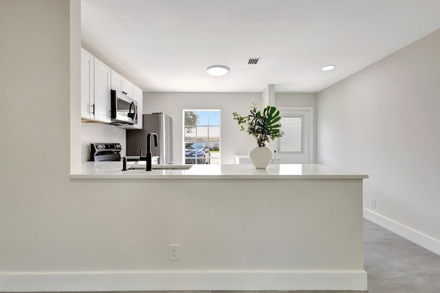 kitchen with stainless steel appliances, finished concrete floors, a peninsula, light countertops, and white cabinets
