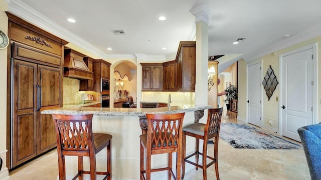 kitchen with custom exhaust hood, light stone counters, crown molding, a kitchen breakfast bar, and a peninsula