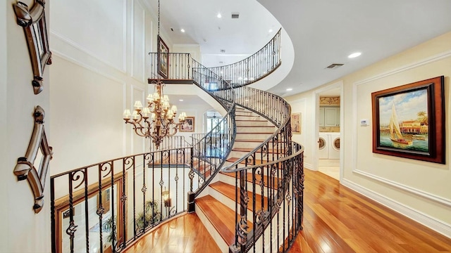 staircase with washing machine and dryer, a chandelier, wood finished floors, arched walkways, and recessed lighting