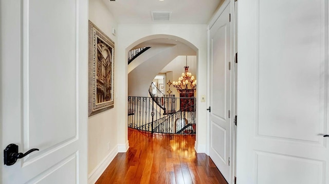 hallway with hardwood / wood-style floors, a chandelier, baseboards, arched walkways, and an upstairs landing