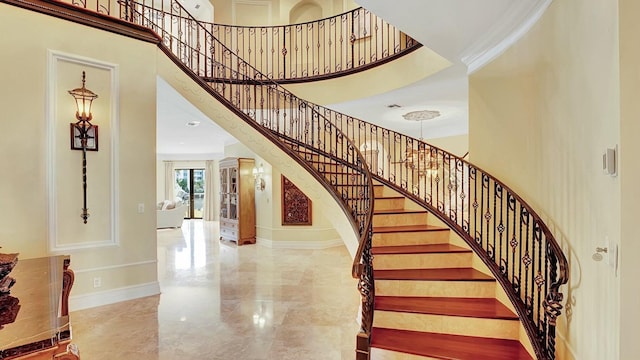 staircase featuring a towering ceiling, marble tiled floors, baseboards, and crown molding