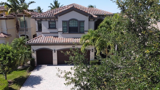 mediterranean / spanish home featuring a tile roof, an attached garage, and stucco siding