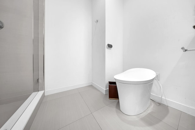 bathroom featuring tiled shower, baseboards, toilet, and tile patterned flooring