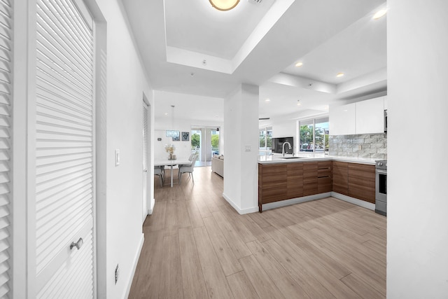 kitchen with modern cabinets, stainless steel electric range, a tray ceiling, light countertops, and light wood-style flooring