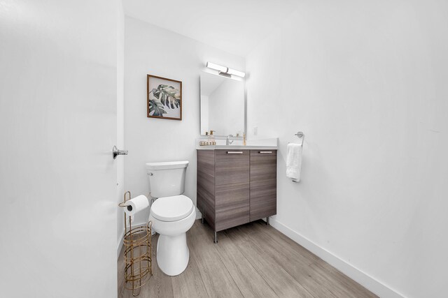 bathroom with wood finished floors, toilet, baseboards, and vanity