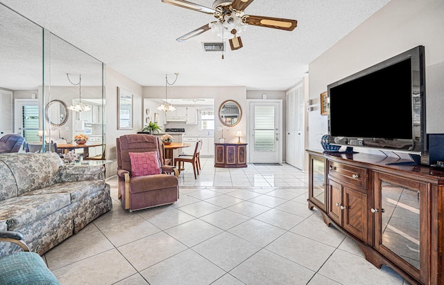 living area with a ceiling fan, a textured ceiling, a chandelier, and light tile patterned floors