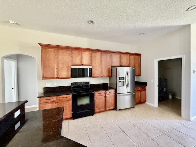 1744 SW Nantucket Ave, Port Saint Lucie, FL 34953 - kitchen with stainless steel appliances, arched walkways, brown cabinetry, light tile patterned floors, and dark stone counters