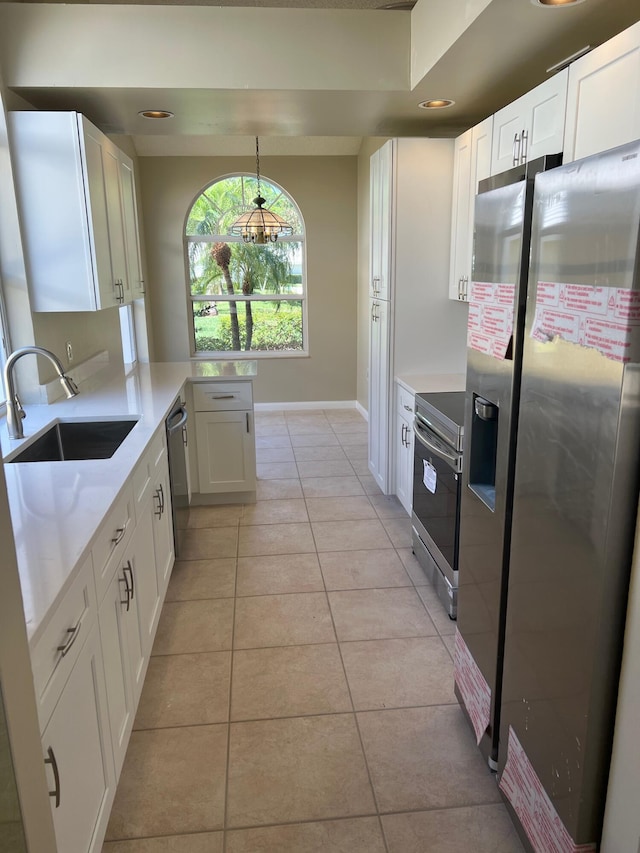 kitchen with appliances with stainless steel finishes, a sink, white cabinetry, light tile patterned flooring, and baseboards