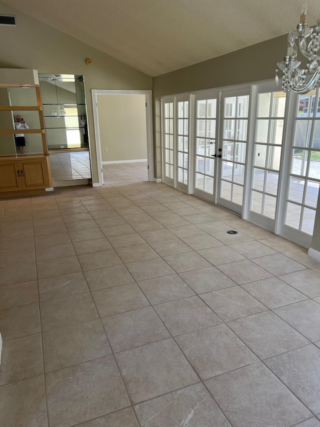empty room with lofted ceiling, a chandelier, light tile patterned flooring, a textured ceiling, and french doors