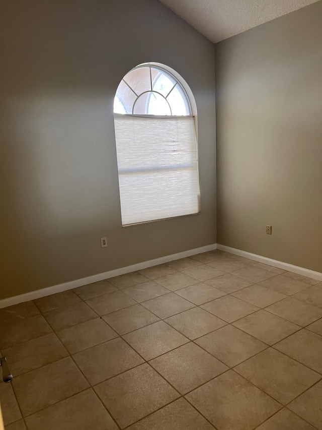 empty room featuring light tile patterned floors, a textured ceiling, baseboards, and lofted ceiling