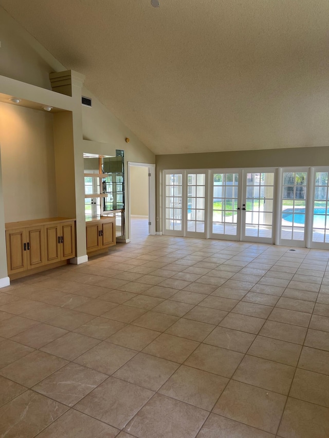 empty room featuring vaulted ceiling, a textured ceiling, healthy amount of natural light, and light tile patterned flooring