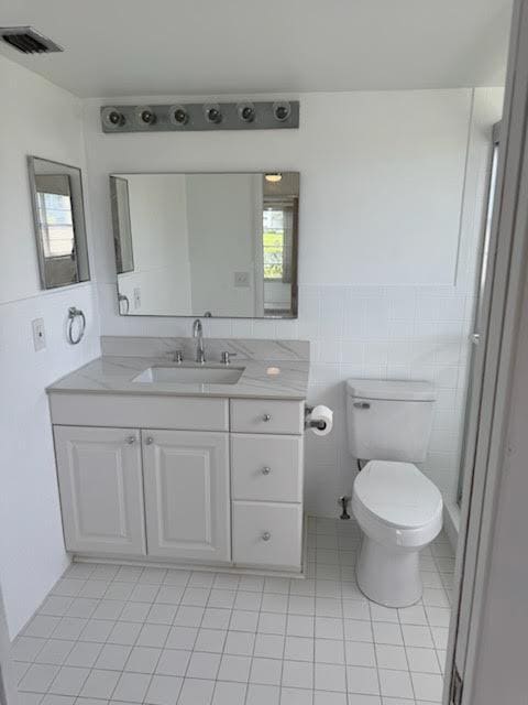 bathroom with toilet, vanity, tile patterned flooring, tile walls, and a wainscoted wall
