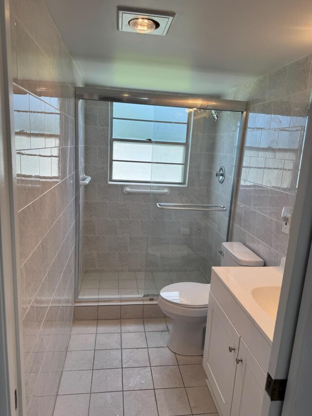 bathroom with tile walls, a stall shower, vanity, toilet, and tile patterned floors