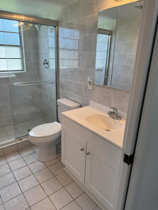full bath with tile walls, a stall shower, toilet, vanity, and tile patterned floors