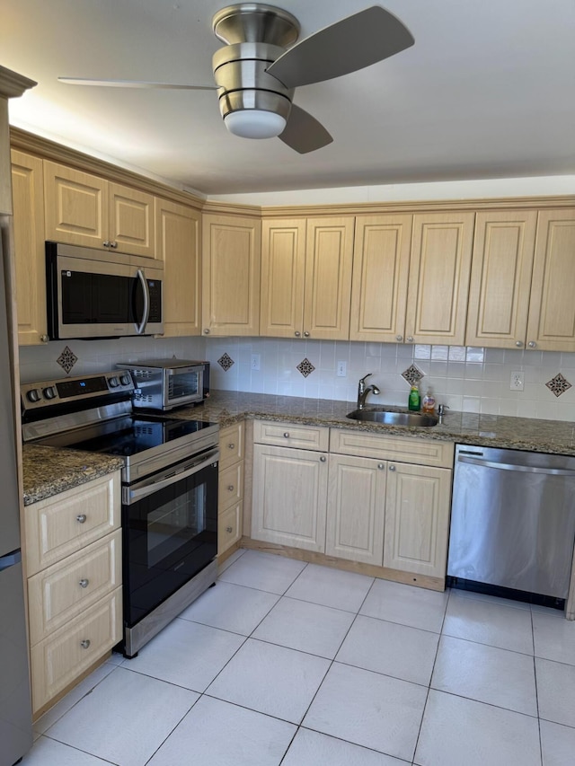 kitchen featuring stainless steel appliances, a ceiling fan, light brown cabinetry, and dark stone countertops