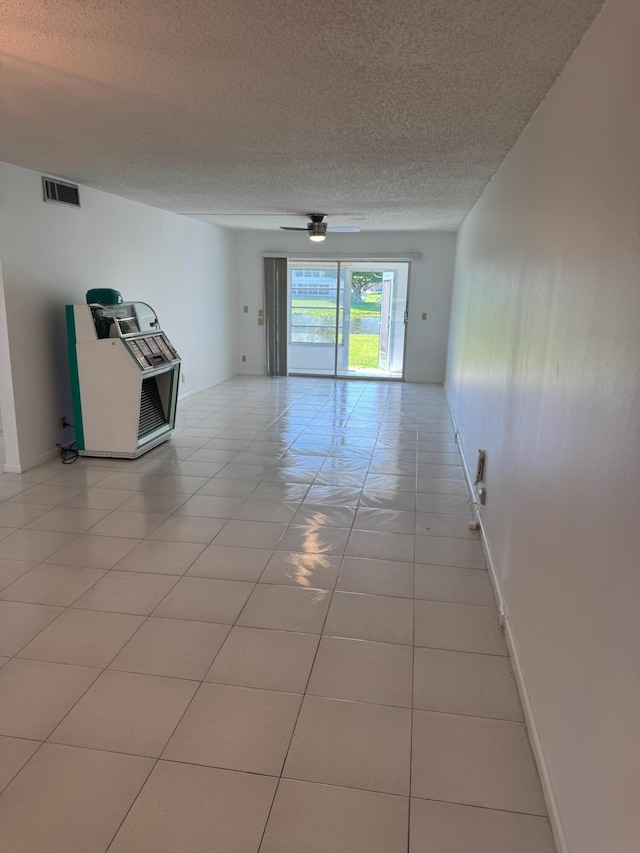 empty room featuring a textured ceiling, a ceiling fan, light tile patterned floors, and baseboards