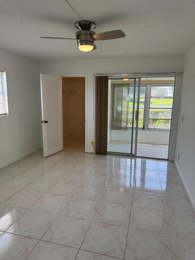 empty room featuring light marble finish floors, a ceiling fan, baseboards, and a textured ceiling