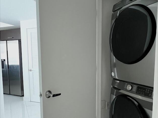laundry area with stacked washer / drying machine and light tile patterned floors