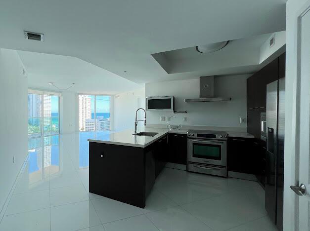 kitchen with appliances with stainless steel finishes, wall chimney range hood, open shelves, a sink, and a peninsula