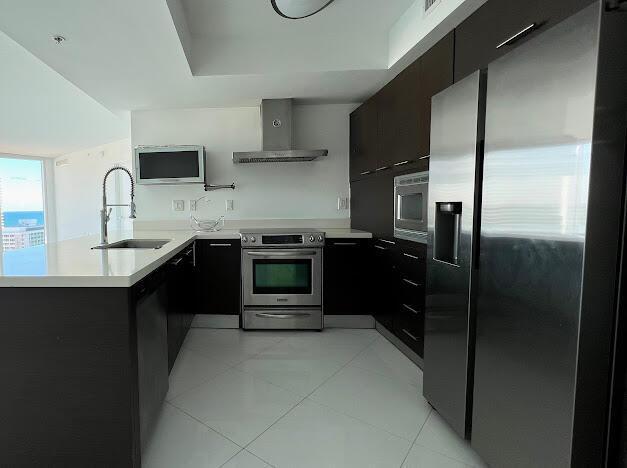 kitchen with stainless steel appliances, wall chimney exhaust hood, modern cabinets, a sink, and light countertops