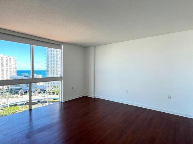 spare room featuring wood finished floors, a city view, baseboards, a water view, and floor to ceiling windows