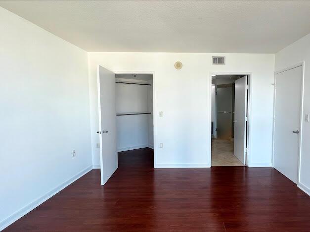 unfurnished bedroom featuring wood finished floors, baseboards, and a walk in closet