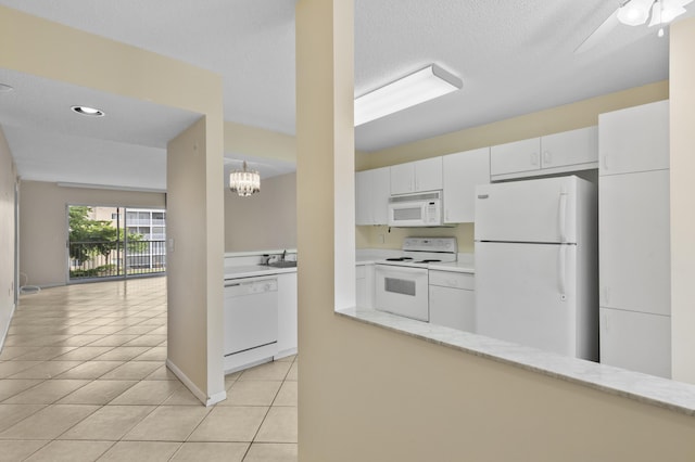 kitchen featuring white appliances, light tile patterned floors, a ceiling fan, white cabinets, and a chandelier