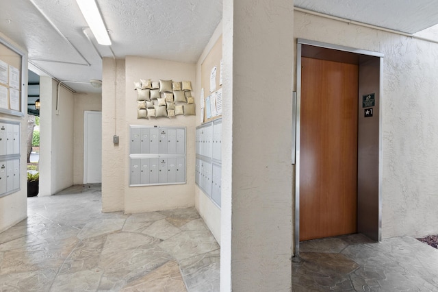 hallway featuring mail area, elevator, stone floors, and a textured wall