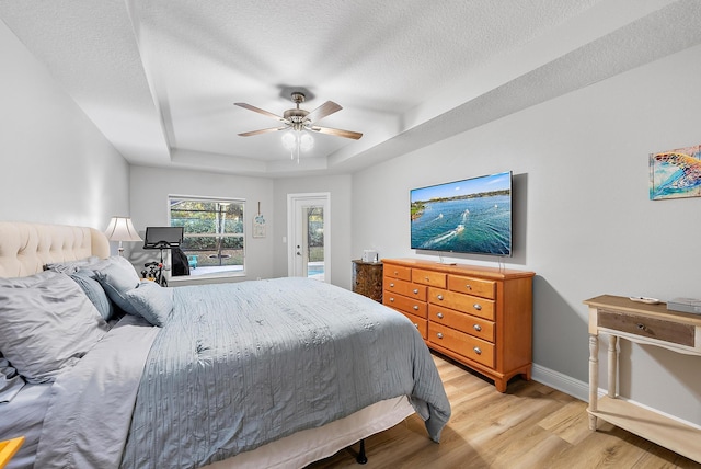 bedroom with a tray ceiling, access to outside, light wood-style flooring, a ceiling fan, and a textured ceiling