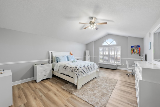 bedroom with vaulted ceiling, light wood-style floors, a textured ceiling, ceiling fan, and baseboards