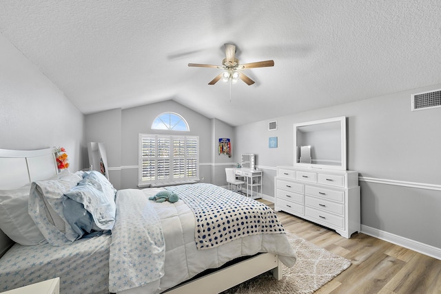bedroom with light wood-style floors, lofted ceiling, ceiling fan, a textured ceiling, and baseboards
