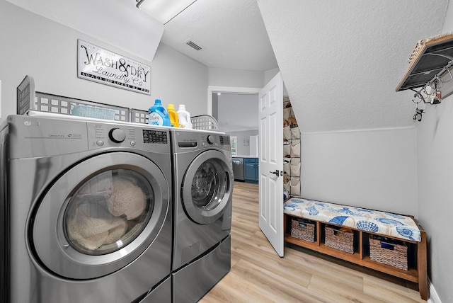 clothes washing area with washer and dryer, light wood finished floors, and a textured ceiling