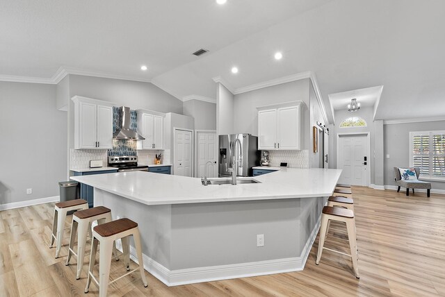 kitchen featuring stainless steel appliances, a kitchen breakfast bar, wall chimney exhaust hood, white cabinetry, and vaulted ceiling