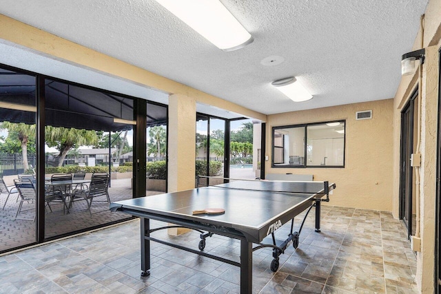 game room featuring a textured ceiling, a textured wall, and stone finish flooring