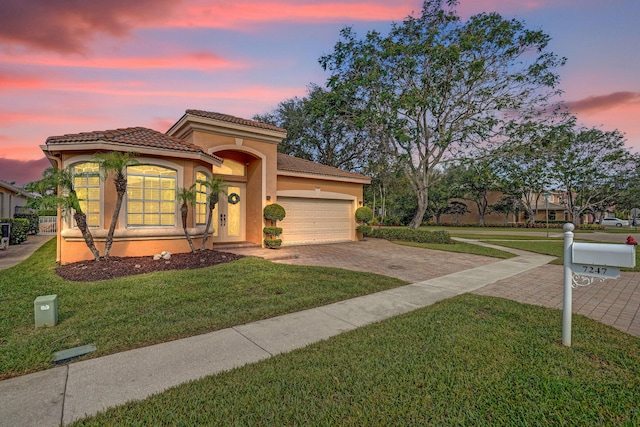 mediterranean / spanish home featuring driveway, stucco siding, a garage, a front yard, and a tile roof