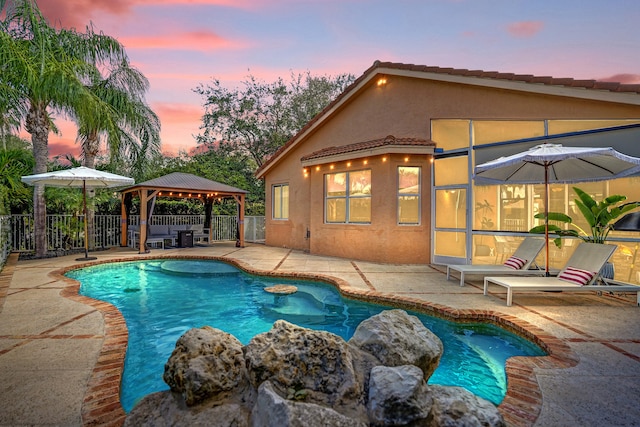 pool at dusk with a gazebo, a patio area, and fence